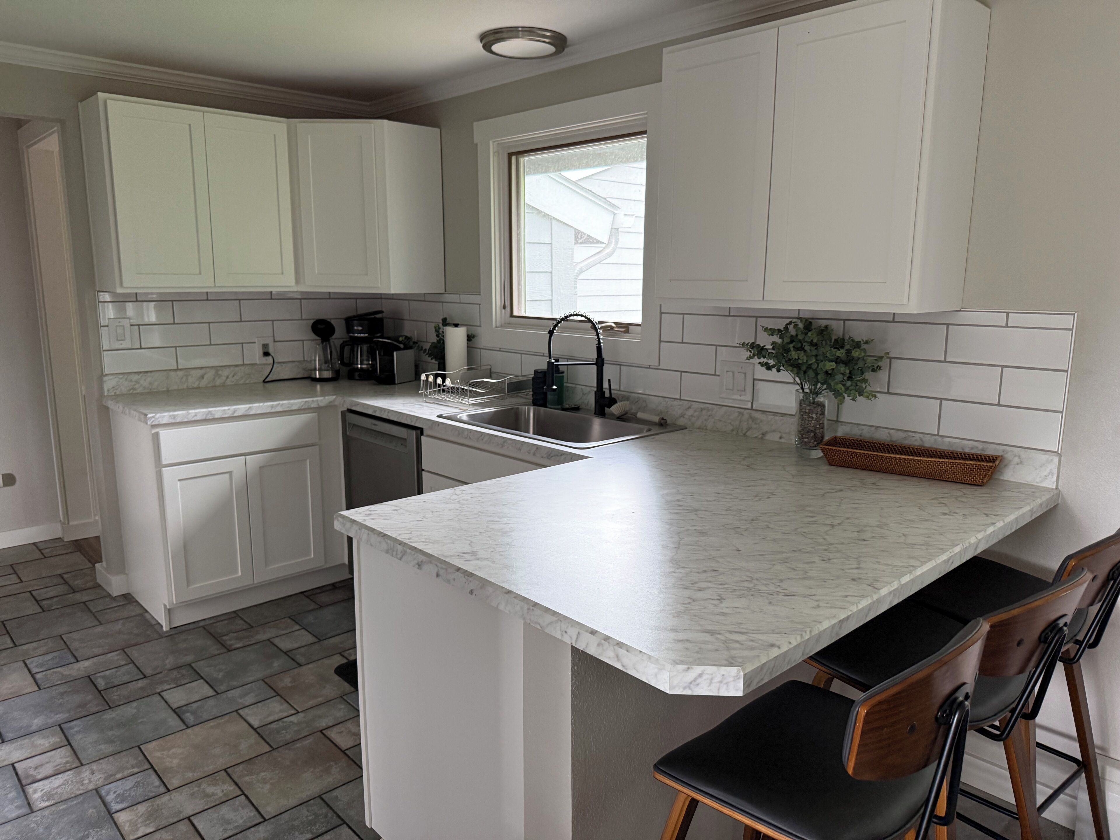 A kitchen with white cabinets, a marble countertop, a window, and a sink.