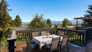 Une terrasse en bois avec une table et des chaises, une pergola et une vue sur les montagnes.