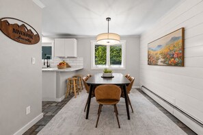 A dining area with a table, chairs, a hanging light fixture, a window with a view, and a wall-mounted sign.