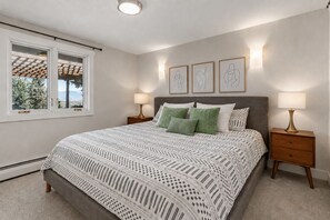 A bedroom with a large bed, two bedside tables, a window with a view, and three wall-mounted artworks.
