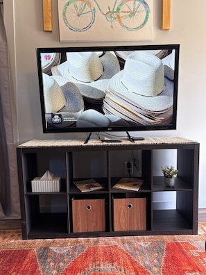 Un televisore su un mobile con piano intrecciato, una rivista su uno scaffale e una piccola pianta in vaso.