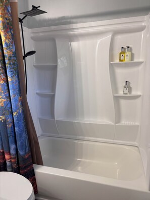 Et badeværelse med badekar, bruser og hylder med toiletartikler.