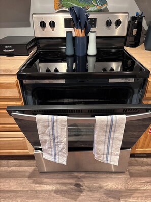 An open stainless steel oven with a tray in the door, a coffee maker, and a knife holder on the countertop.