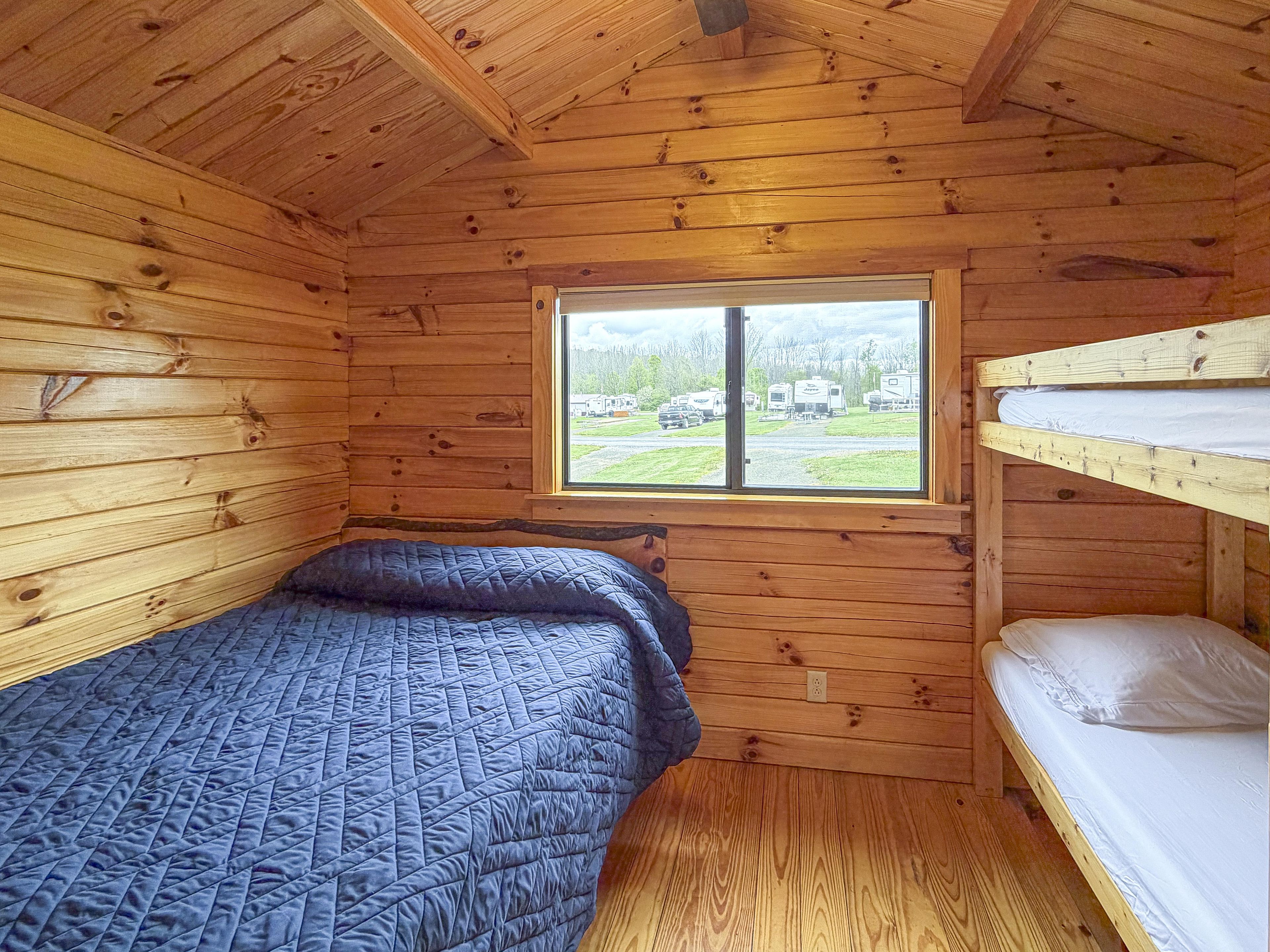 A cabin with a bunk bed, a window with a view of a campground, and wooden walls.