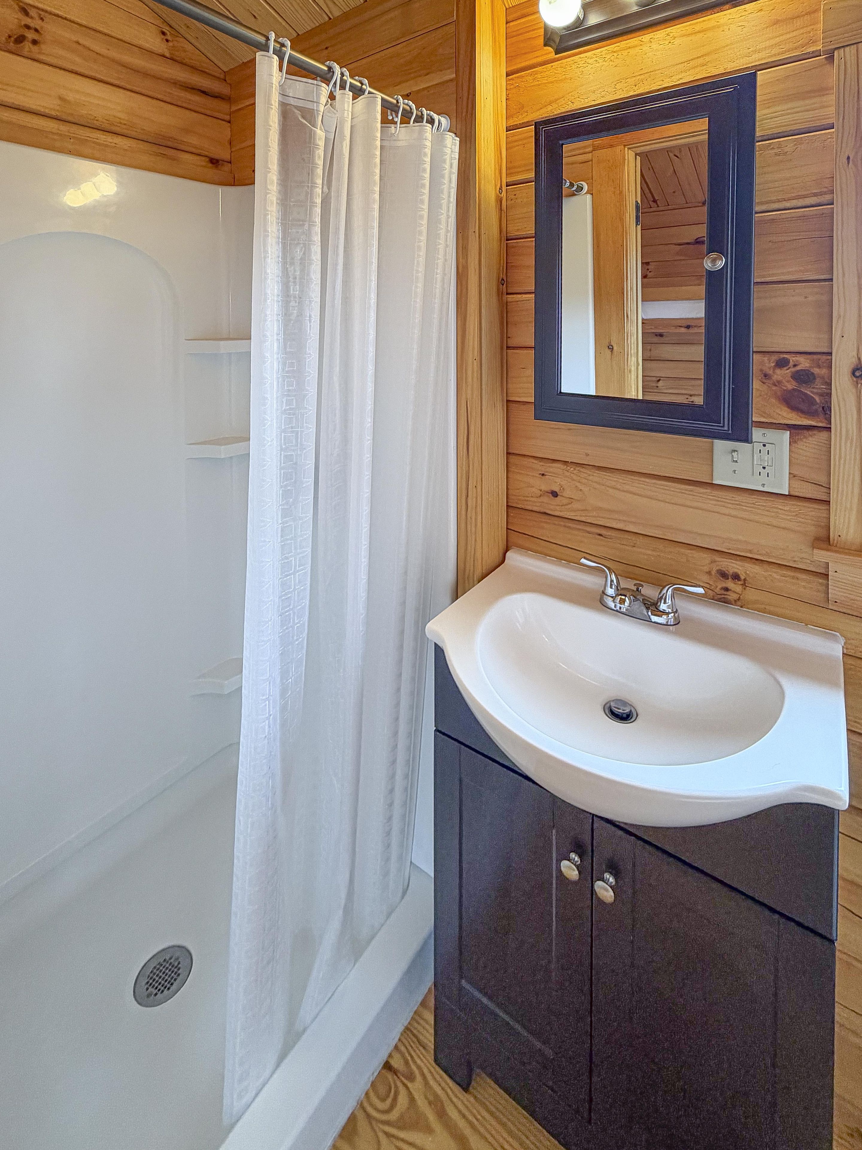 A bathroom with a bathtub, a shower curtain, a sink, and a mirror.