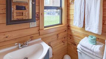 Une salle de bain rustique, aménagée dans une cabane en bois, avec un lavabo, un miroir, une fenêtre et des toilettes.