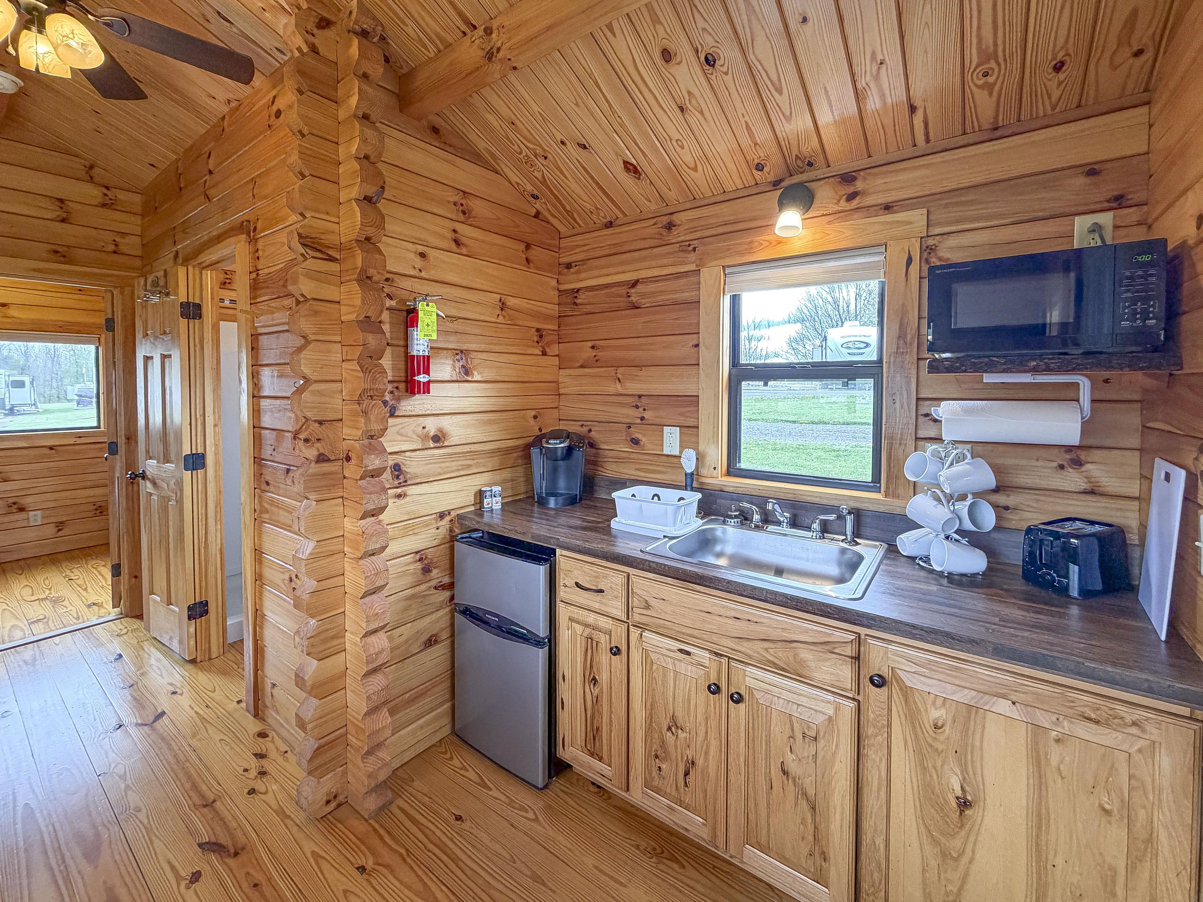 Une cuisine aménagée dans une cabane en bois, équipée d’un réfrigérateur, d’un évier, d’un four à micro-ondes et d’une machine à café.