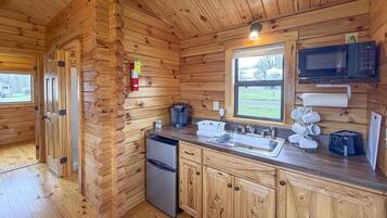 Une cuisine aménagée dans une cabane en bois, équipée d’un réfrigérateur, d’un évier, d’un four à micro-ondes et d’une machine à café.