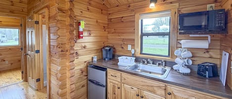 Eine Holzhütte mit einer Küche, inklusive Kühlschrank, Spüle, Mikrowelle und Kaffeemaschine.