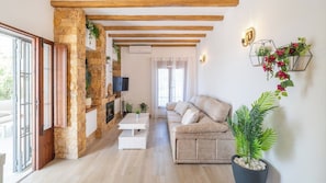 Ein Wohnzimmer mit Steinwand, Holzbalken, einem weißen Sofa, einem Couchtisch und Topfpflanzen.