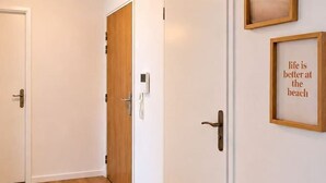 Un couloir doté d’un plancher en bois, de murs blancs et de deux portes, dont l’une est ornée d’un panneau en bois et l’autre d’un panneau blanc. Deux tableaux encadrés sont accrochés au mur.