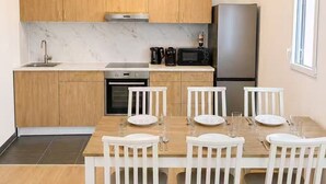 Une cuisine moderne avec des meubles en bois, un pare-feu en marbre et un coin repas comprenant des chaises blanches et une table en bois.