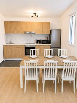 A modern kitchen with wooden cabinets, a marble backsplash, and a dining area with white chairs and a wooden table. - Brand New Family Apartment, Terrace & Parking, 15 min from Disneyland (Bussy-Saint-Georges)
