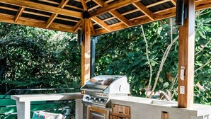 Une terrasse extérieure dotée d’un plafond en bois, d’un barbecue encastré et de meubles en osier.