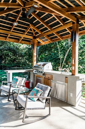 Eine Terrasse im Freien mit Holzboden, integriertem Grill und Korbmöbeln.