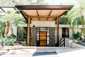 Ein modernes Gebäude mit einem Holz-Pergola-Eingang, einer Steinmauer und einem Betonweg, der zur Tür führt.
