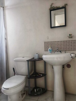 Un baño con inodoro, lavamanos y un pequeño estante con artículos de aseo.