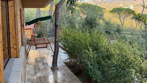 A wooden porch with a swing, a tiled floor, and a view of a hilly landscape.