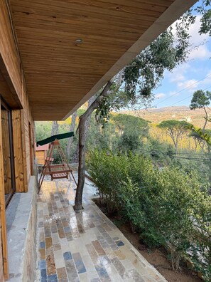 A wooden porch with a swing, a tiled floor, and a view of a hilly landscape.
