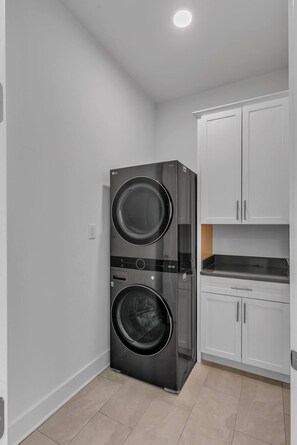 A compact laundry room with a front-loading washer and dryer, white cabinets, and a tiled floor. - Comfort, Space & Convenience – Beautiful 3-Bedroom (Hendersonville)