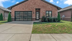 A single-story brick building with a large garage door, a small front porch, and a well-maintained lawn. - Comfort, Space & Convenience – Beautiful 3-Bedroom (Hendersonville)