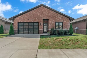 A single-story brick building with a large garage door, a small front porch, and a well-maintained lawn. - Comfort, Space & Convenience – Beautiful 3-Bedroom (Hendersonville)