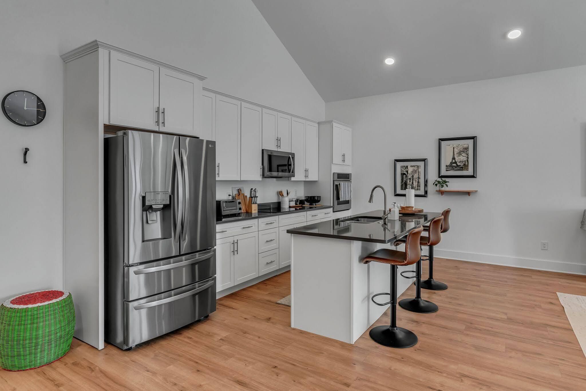 A modern kitchen with a stainless steel refrigerator, white cabinets, a microwave, and a bar area with stools.