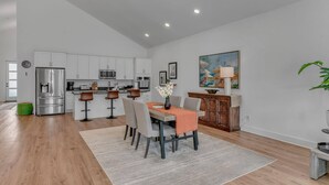 A modern kitchen with white cabinets, stainless steel appliances, and a dining area with a table set for four. - Comfort, Space & Convenience – Beautiful 3-Bedroom (Hendersonville)