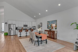 A modern kitchen with white cabinets, stainless steel appliances, and a dining area with a table set for four. - Comfort, Space & Convenience – Beautiful 3-Bedroom (Hendersonville)