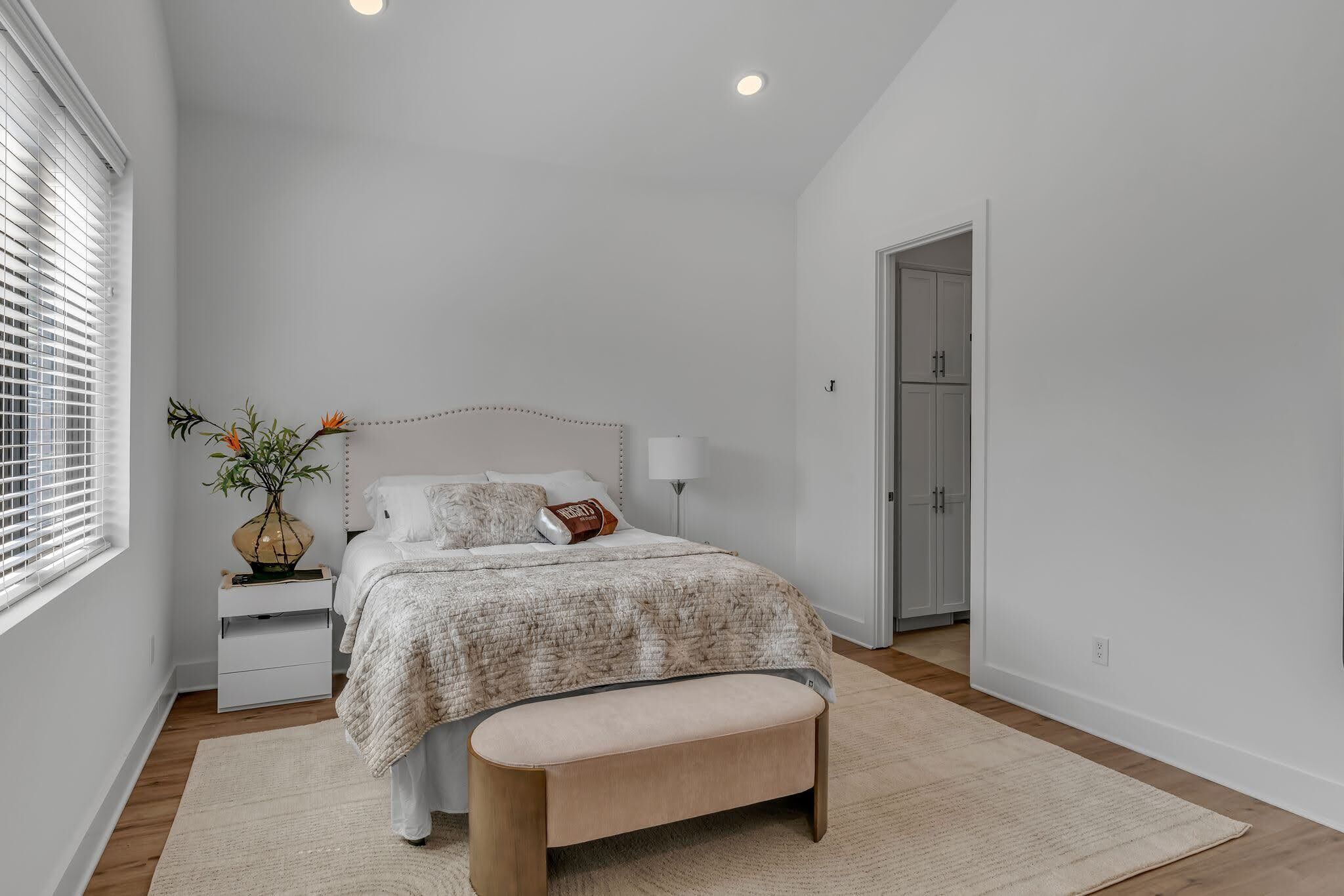 Quarto com cama, mesa de cabeceira, abajur e janela com persianas.
