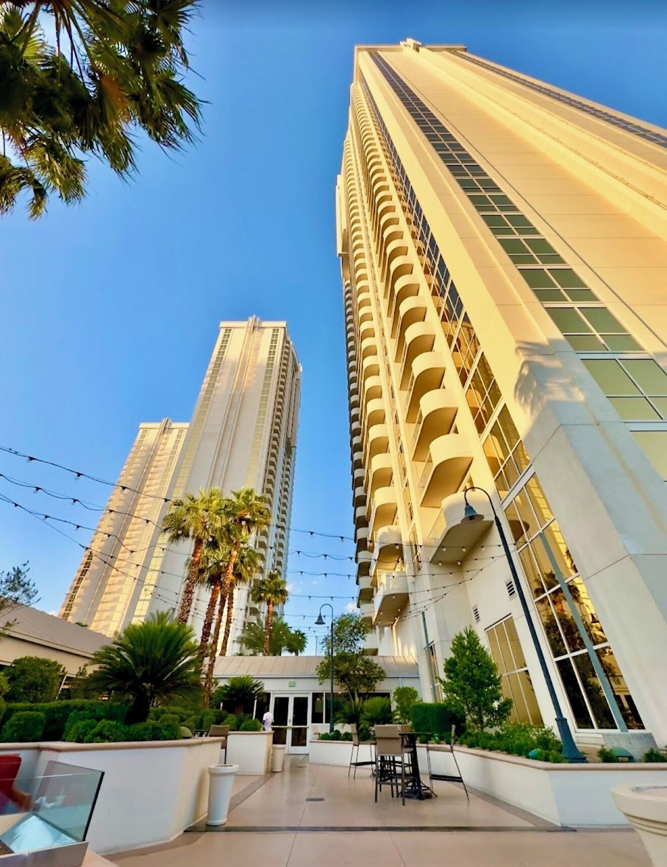 A high-rise hotel with multiple balconies, a central courtyard with seating, and palm trees.