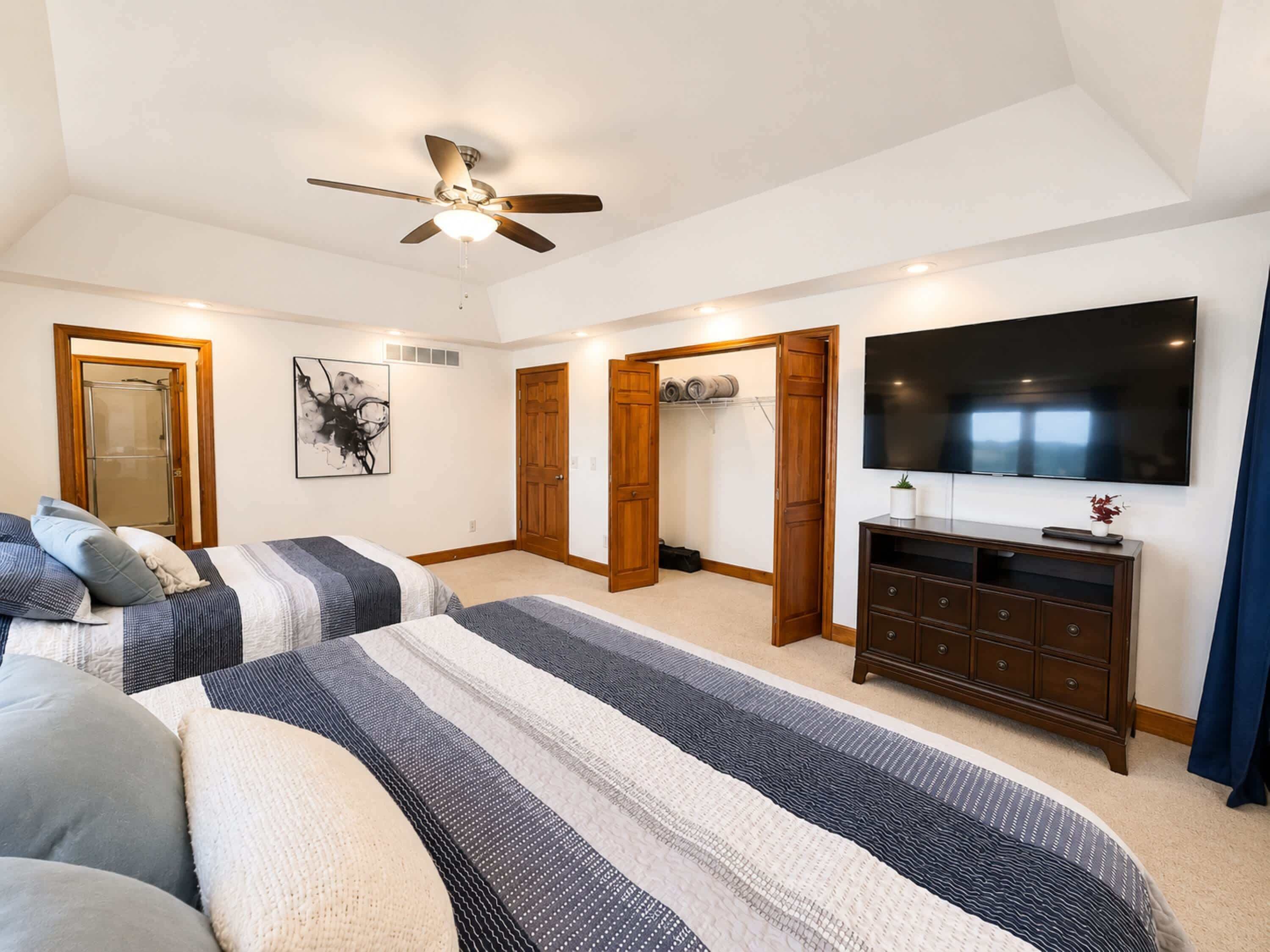 A bedroom with two beds, a ceiling fan, a TV, and a walk-in closet.