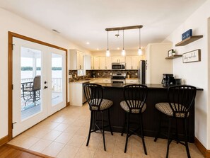 A kitchen with a bar area, a dining table with chairs, and a view through a glass door to an outdoor deck. - It's A Shore Thing - Boat Slips and Hot Tub (Osage Beach)