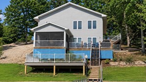 A two-story house with a covered porch, a deck, and a staircase leading to the upper level. - It's A Shore Thing - Boat Slips and Hot Tub (Osage Beach)