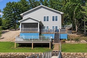 A two-story house with a covered porch, a deck, and a staircase leading to the upper level. - It's A Shore Thing - Boat Slips and Hot Tub (Osage Beach)