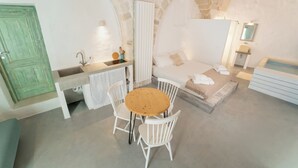 Una habitación con pared de piedra, una cama, un lavabo, una mesa con sillas y un espejo.