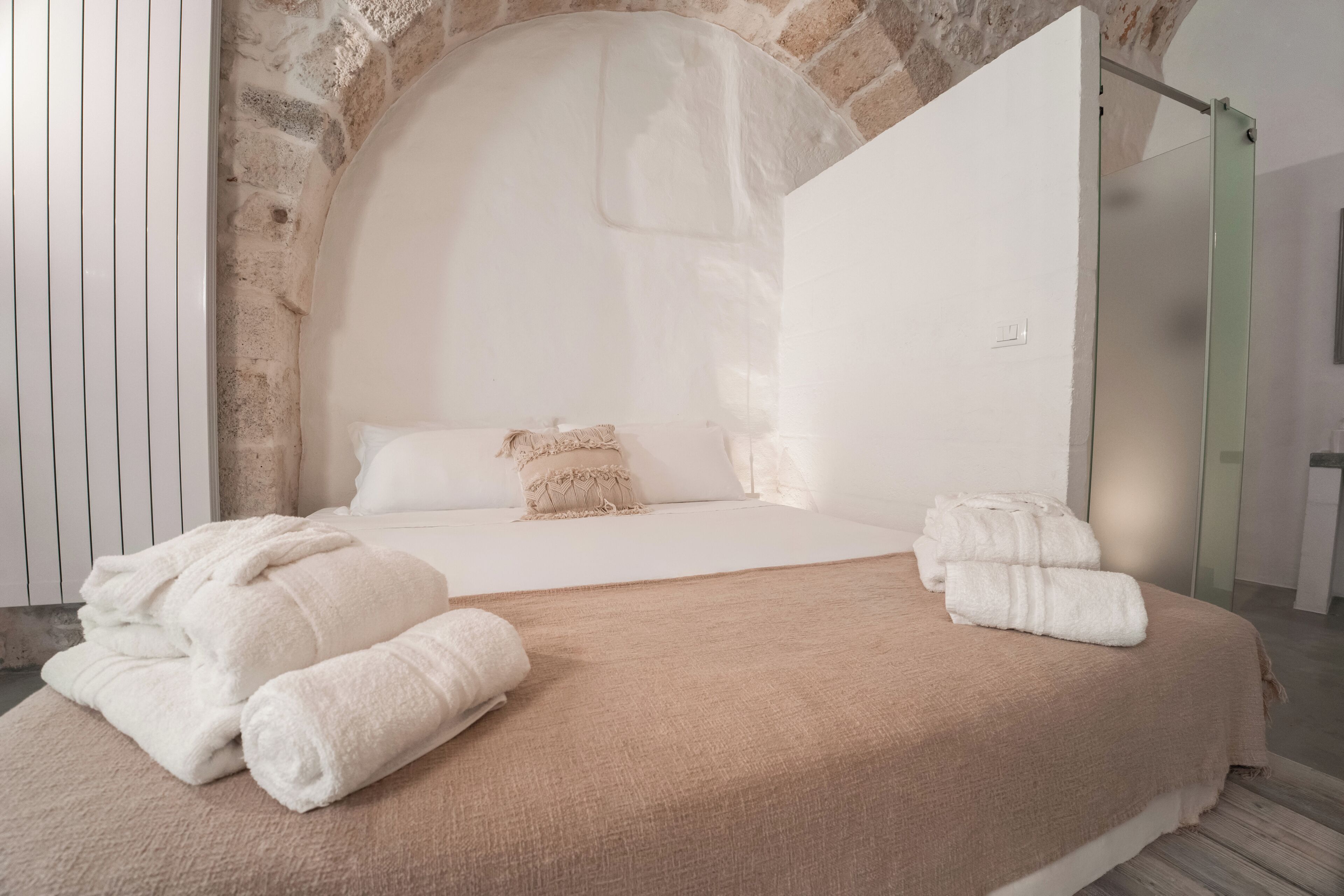 A modern bedroom with a stone wall, a bed with white linens, and a glass shower enclosure.