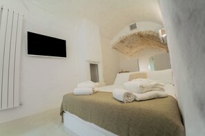 Une chambre d’hôtel moderne équipée d’un lit, de serviettes, d’une télévision et d’une arche en pierre.