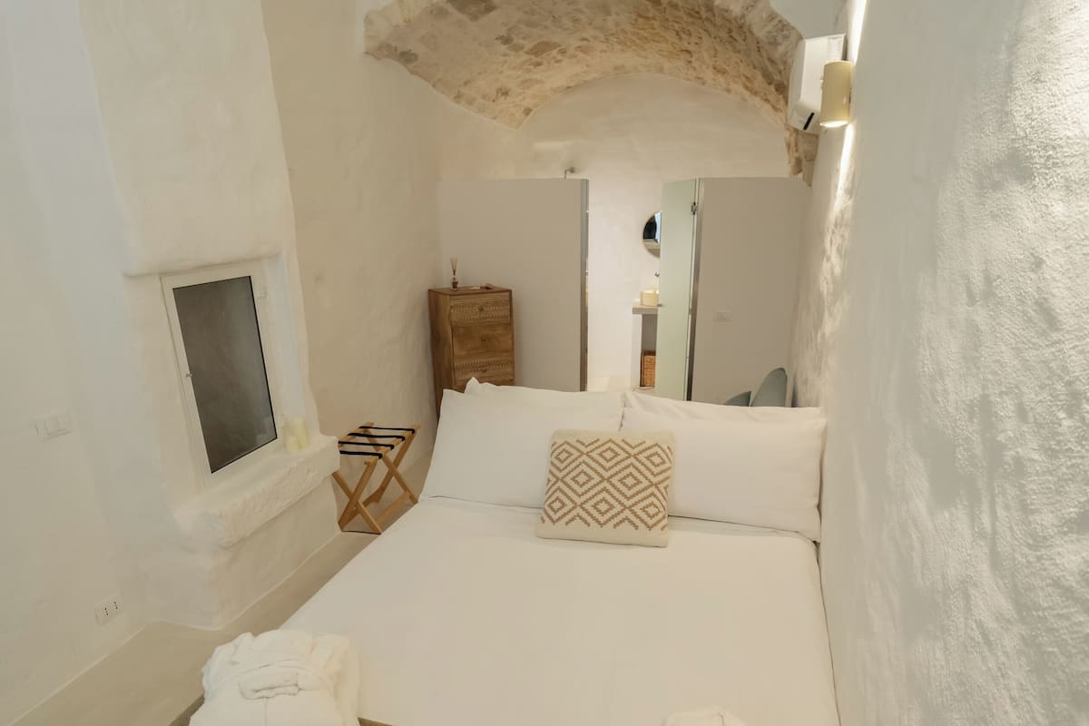 Un dormitorio con cama, toallas, una mesita de noche de madera, un espejo y un techo abovedado.