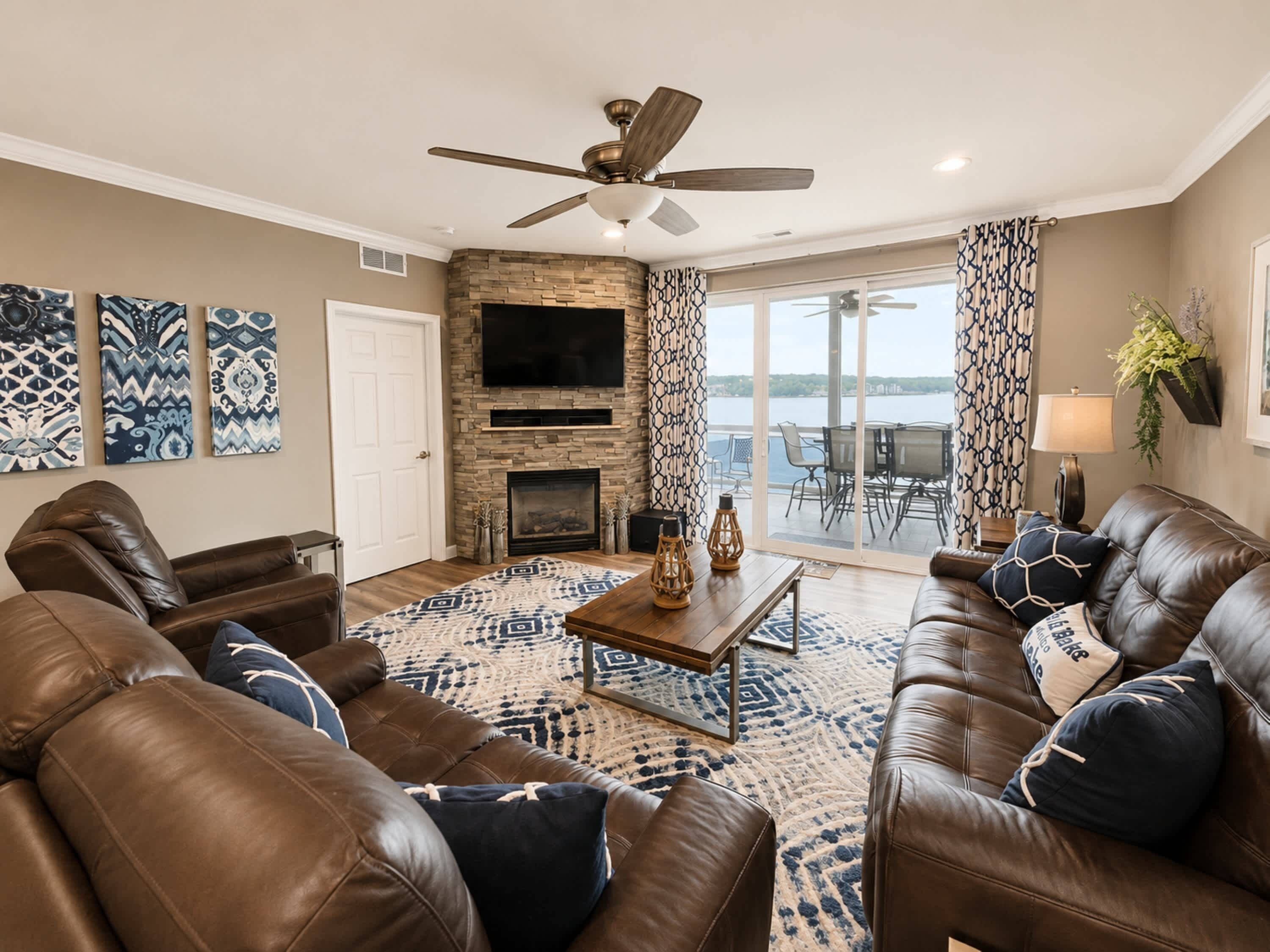 A living room with leather sofas, a fireplace, a ceiling fan, and a large TV.
