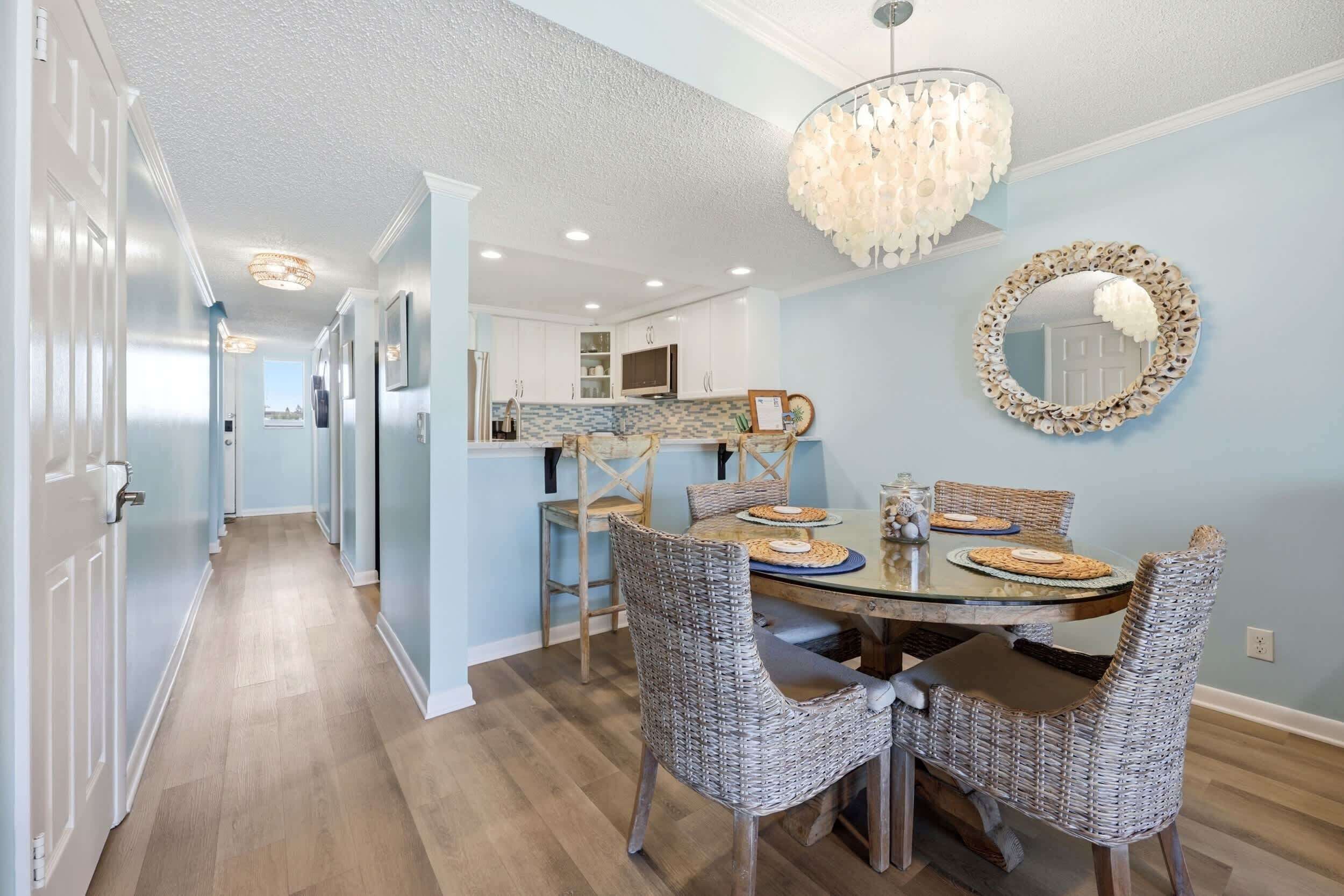 A dining area with wicker chairs, a glass table, and a decorative mirror on the wall.