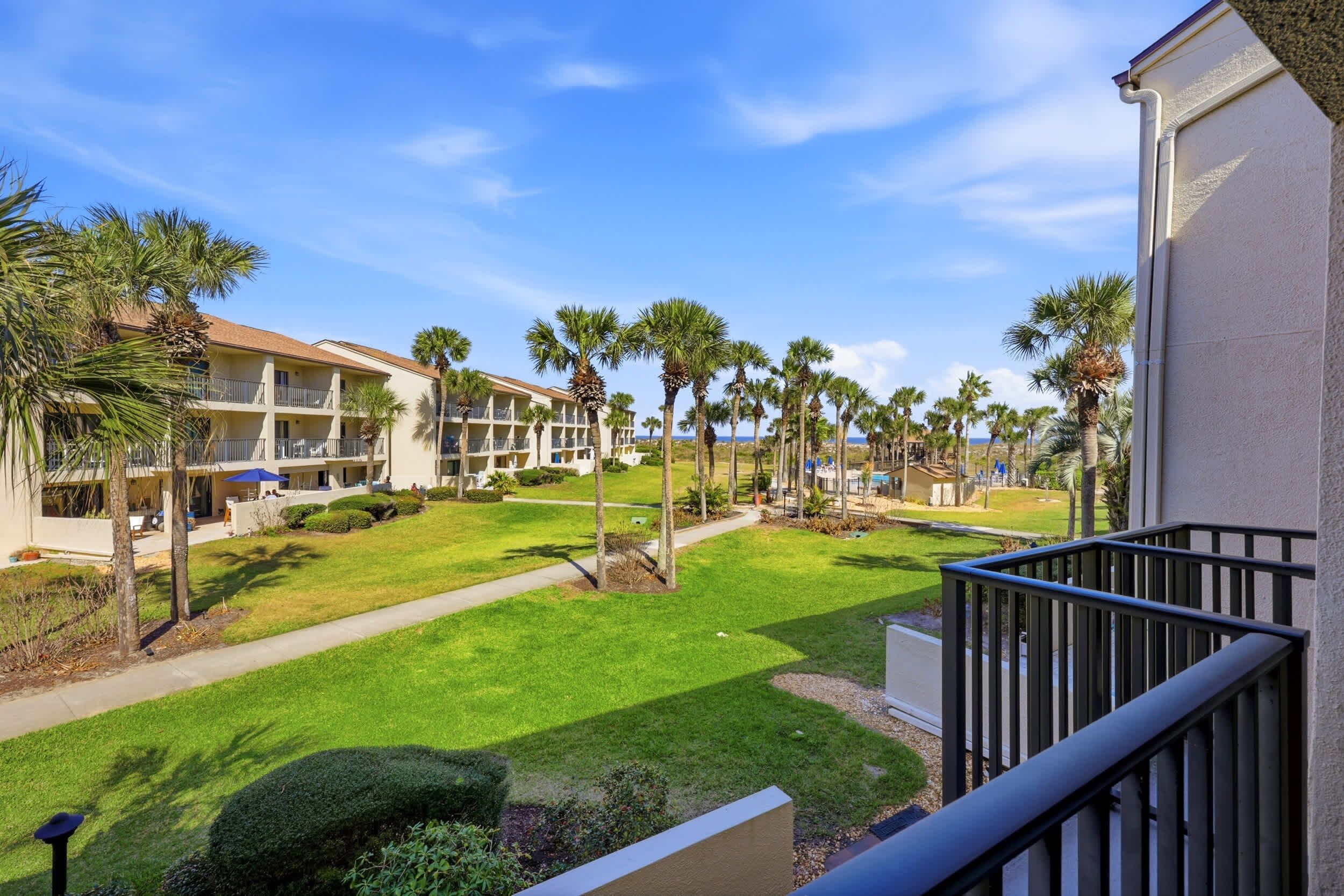 A hotel with a well-maintained lawn, palm trees, and a clear view of the ocean.