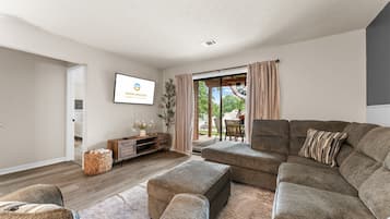 Una sala de estar moderna con un sofá seccional, un televisor de pantalla plana y un ventanal corredizo que da a un patio exterior.