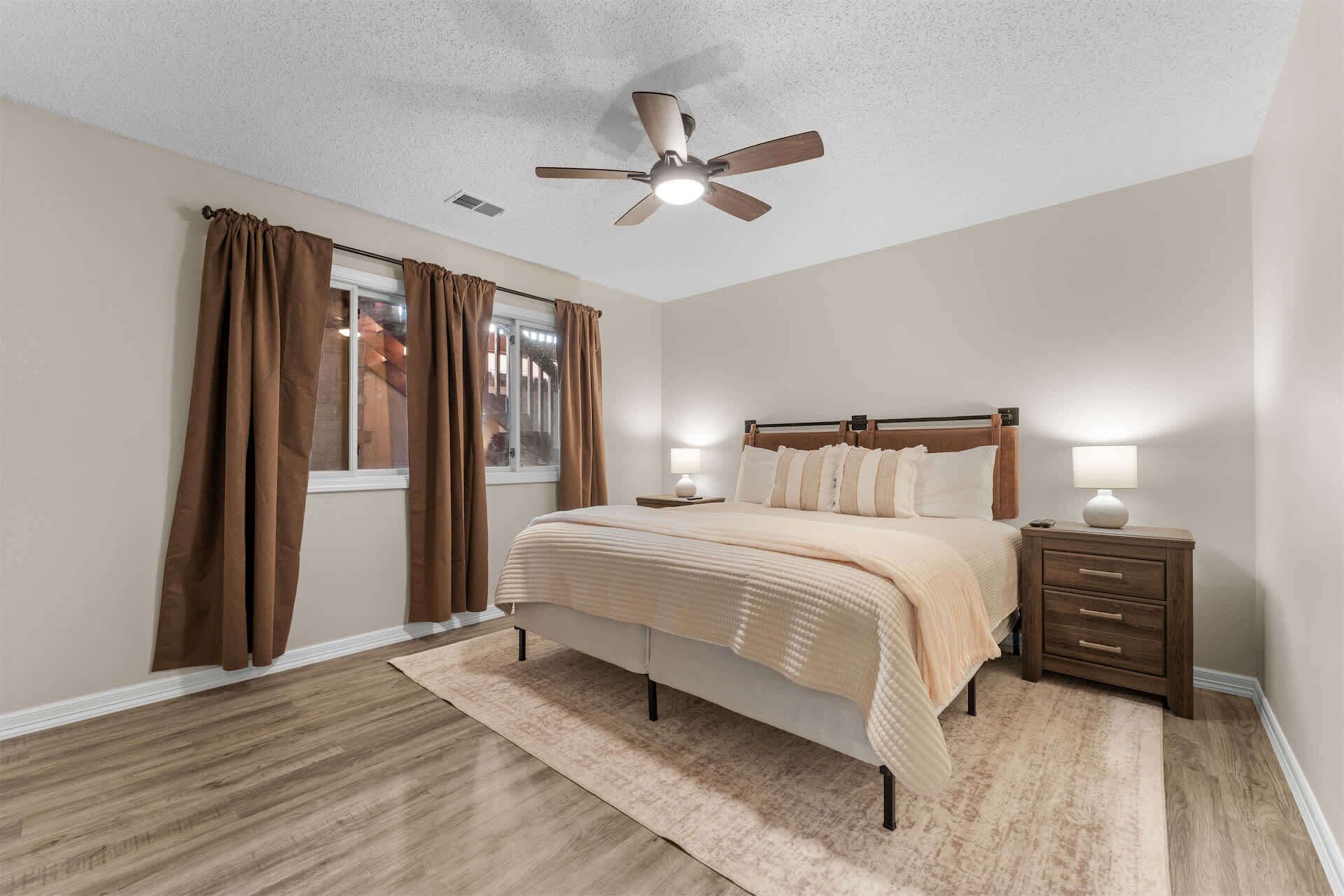 A bedroom with a bed, nightstands, a ceiling fan, and a window with curtains.