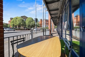 A covered outdoor seating area with a table and chairs, a view of a street with cars, and buildings in the background. - Welcome to "your space" with Private Patio (Birmingham)