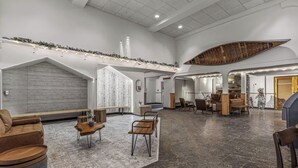Een ruime lobby met een hoge plafond, een decoratieve houten boot en een zithoek met banken en tafels.