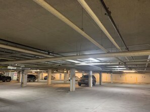 Un garaje subterráneo con pilares de hormigón, tuberías en el techo y varios coches aparcados.