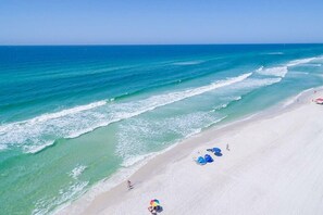 Ein Strand mit klarem türkisblauem Wasser, weißem Sand und Sonnenschirmen.