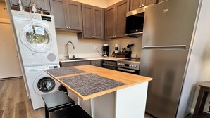 A compact kitchen with a built-in washer, a stainless steel refrigerator, and a small dining area with stools. - 8th Floor Studio Rental with High Ceilings! (Spokane)