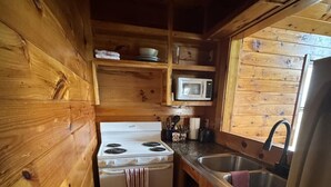 Una cocina compacta con paredes de madera, una estufa blanca, un microondas y un fregadero.
